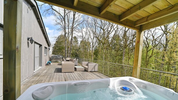 A wooden deck with a hot tub, outdoor furniture, and a view of trees.