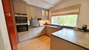 A modern kitchen with wooden flooring, built-in appliances, and a large window with a view of trees.