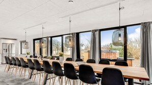 A modern dining area with a long wooden table, black chairs, and large windows offering a view of the outdoors. - 4 Star Holiday Home in Ulfborg (Ulfborg)
