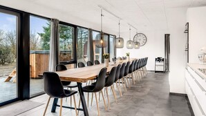 A modern dining area with a long wooden table, black chairs, and large windows offering a view of the outdoors. - 4 Star Holiday Home in Ulfborg (Ulfborg)