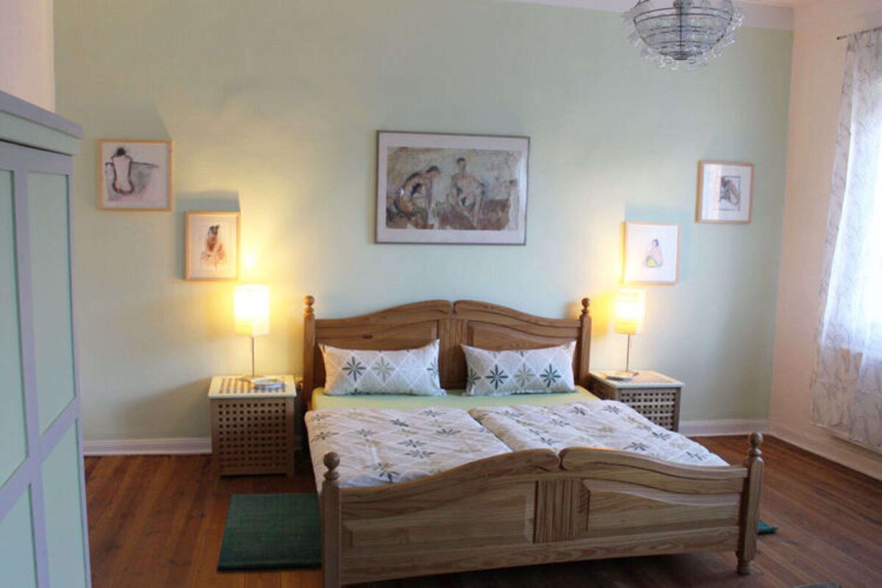 A bedroom with a wooden bed, two bedside tables, a green rug, and framed artwork on the walls.