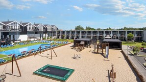 A pool area with lounge chairs and a trampoline, surrounded by a building with multiple balconies. - 4 Person Holiday Home on Holiday Park in Glesborg (Glesborg)