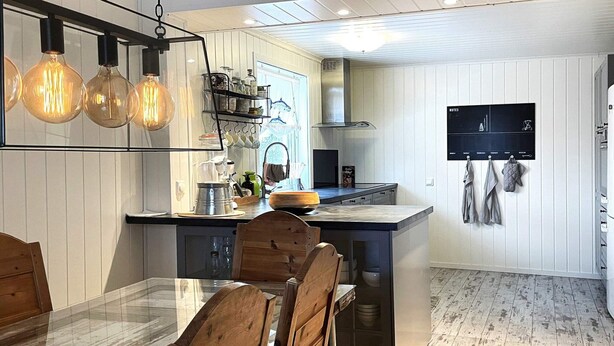 Une cuisine moderne dotée d’un îlot central, de chaises en bois et de luminaires suspendus.