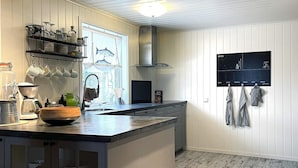 Une cuisine moderne dotée d’un grand îlot central, de tasses suspendues, d’un tableau noir affichant le programme de la semaine et offrant une vue sur l’extérieur grâce à une fenêtre.