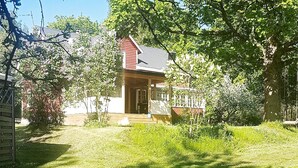 Une petite maison dotée d’une terrasse en bois, entourée d’une végétation luxuriante et d’arbres.