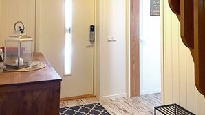 Une chambre d’hôtel avec un bureau en bois, une table de chevet, une petite table avec un verre et une bouteille, une porte avec une poignée et un panneau fixé au mur.