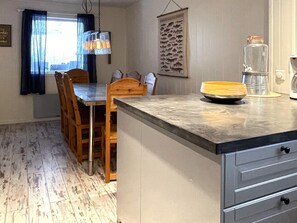 Une cuisine compacte avec une table à manger en bois, un luminaire suspendu et une décoration murale sur le thème des poissons.