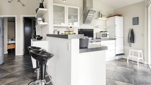 A modern kitchen with a central island, white cabinetry, and a black bar stool. - 4 Star Holiday Home in Sydals (Sydals)