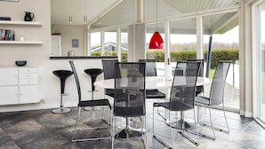 A modern dining area with a white table and black chairs, large windows, and a view of the outdoors. - 4 Star Holiday Home in Sydals (Sydals)