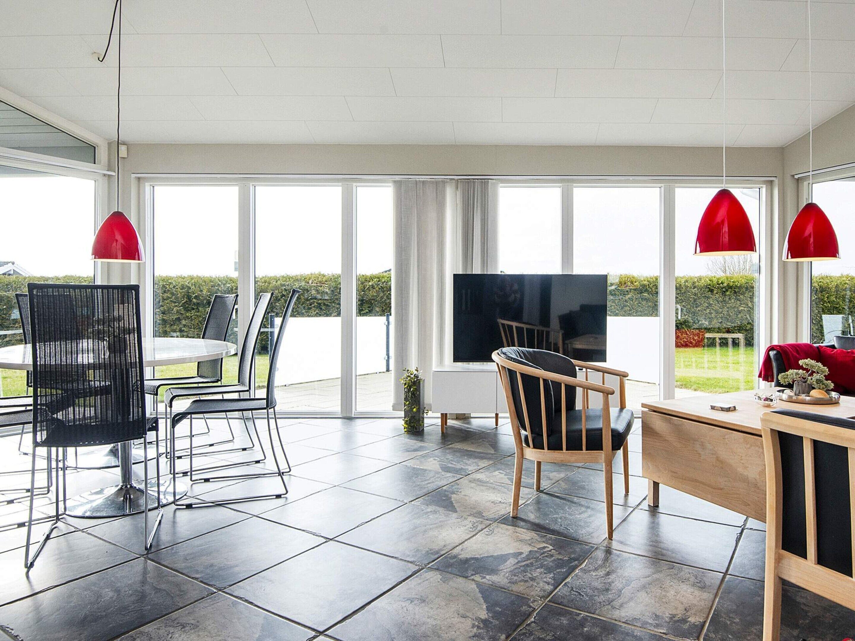 A spacious living area with a dining table, chairs, a TV, and large windows offering a view of the outdoors.