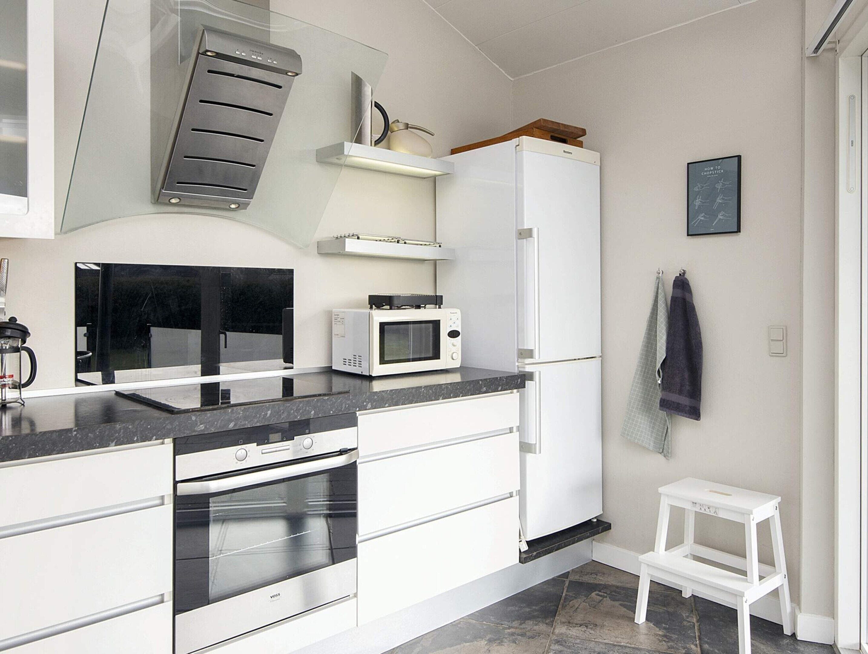 A modern kitchen with white cabinetry, a microwave, a built-in oven, and a refrigerator.