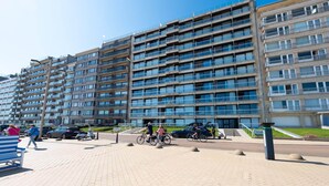 Un edifici residencial de diverses plantes amb balcons i una passera pavimentada al davant.