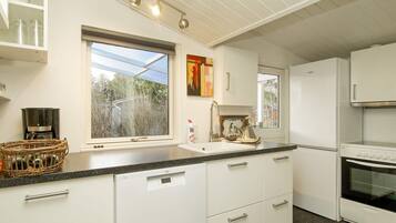 A modern kitchen with white cabinetry, a built-in oven, a coffee maker, and a window with a view of trees.