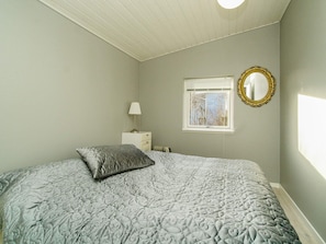 Un dormitorio con cama, mesita de noche, lámpara, ventana y espejo.