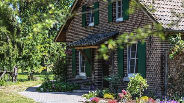 A brick house with green shutters, a porch, and a garden with various flowers. - Lovely Apartment in Straelen (Straelen)