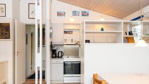 A compact kitchen with a stove, oven, and coffee maker, a dining area with a table and chairs, and a hallway with a door leading to another room. - 8 Person Holiday Home in Farvang (Farvang)