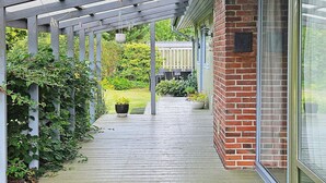 A covered outdoor area with a wooden deck, potted plants, and a brick wall. - 8 Person Holiday Home in Farvang (Farvang)