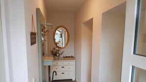Un couloir étroit avec une commode blanche, un miroir et une petite plante.