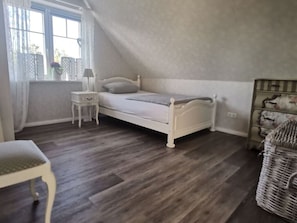 A bedroom with a single bed, a nightstand, a chair, and a wicker basket.