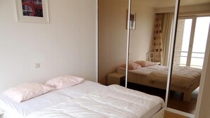 A bedroom with a bed, a mirror, and a window. - Apartment in Nieuwpoort With Coastal Views (Nieuwpoort)