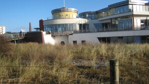A modern building with a flag on top, a circular structure, and a flat roof. - - 2 min zum Strand (Borkum)