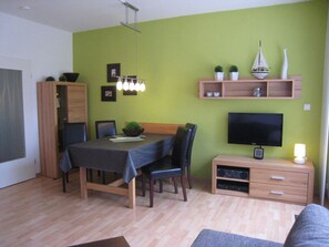 A dining area with a table, chairs, and a television on a stand. - - 2 min zum Strand (Borkum)
