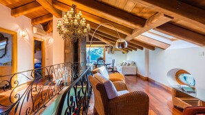 Een ruime loft met hoge plafonds, zichtbare houten balken, een balkonhek van ijzer en een grote kroonluchter.