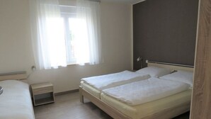 Ein Schlafzimmer mit zwei Betten, einem Nachttisch, einem Fenster mit Vorhängen und Holzboden.