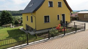 Ein gelbes Haus mit dunklem Dach, einer kleinen Veranda und einem schwarzen Metallzaun.