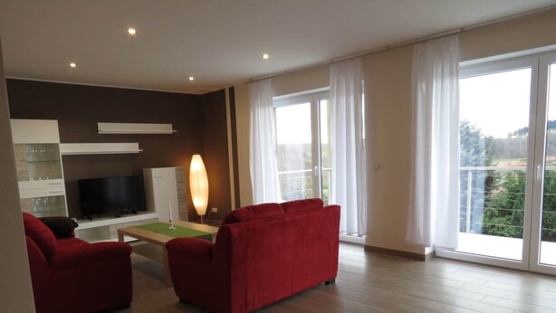 Ein modernes Wohnzimmer mit einem Flachbildfernseher, einem roten Sofa und einem Tisch mit einer Lampe.