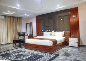 A modern hotel bedroom with a large bed, a bedside table, a chair, a mirror, and a decorative wall panel.