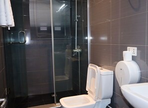 A modern bathroom with a glass shower enclosure, a toilet, and a hand dryer.