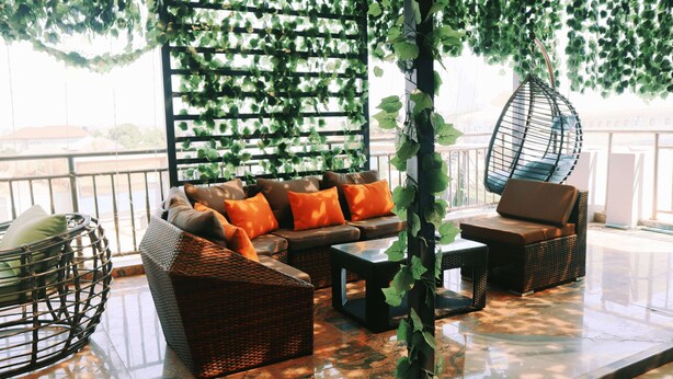 Un espacio al aire libre con luz solar, muebles de mimbre, una silla colgante y vistas a un cuerpo de agua.
