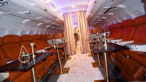 Cabina de avión con filas de asientos de cuero, compartimentos superiores y un pasillo central.