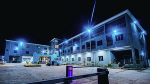 Un hotel de varios pisos con entrada central, estacionamiento exterior y un acceso con puerta de seguridad.