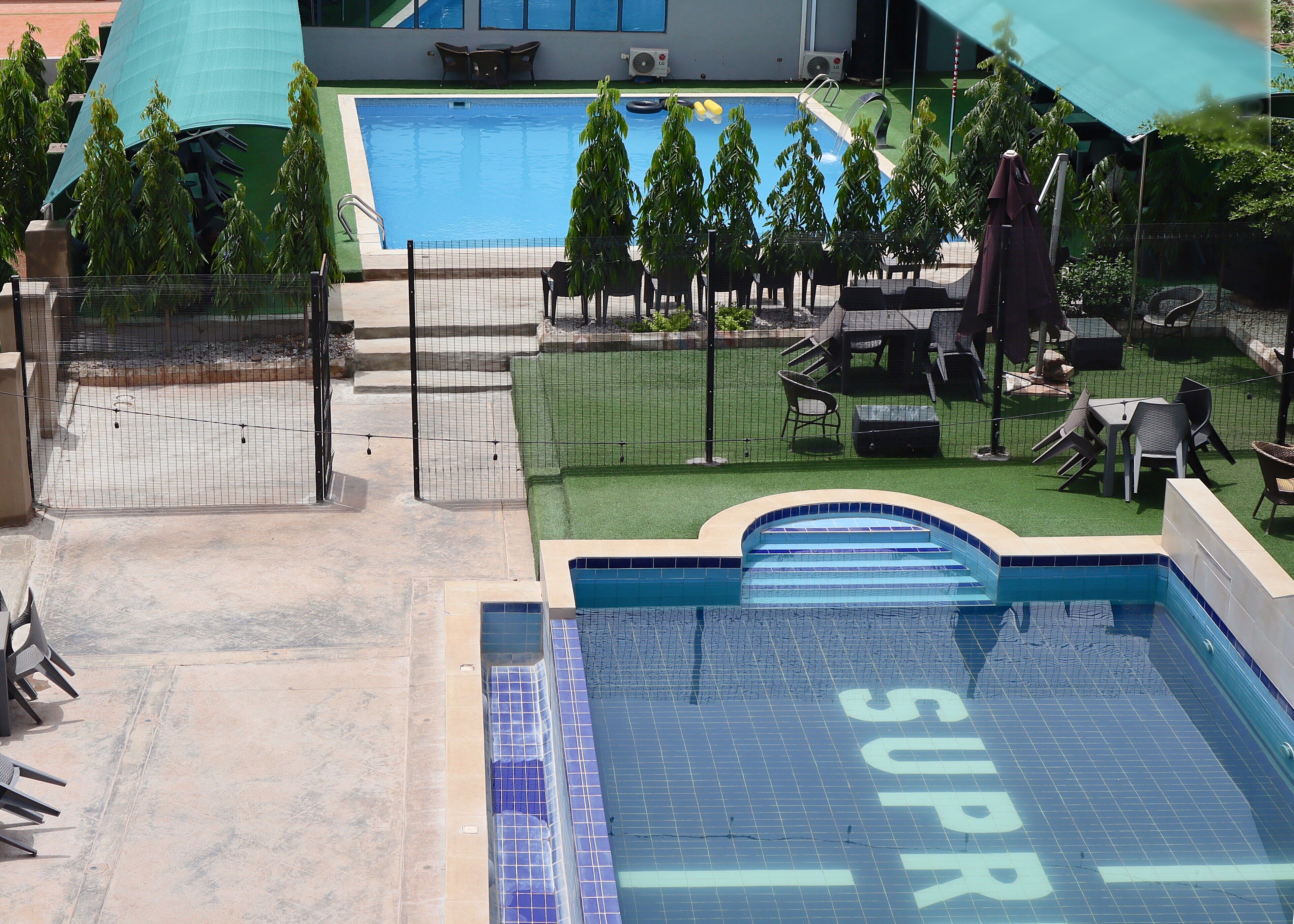 Uma piscina com uma placa 'SUPRI', cercada por uma grade, cadeiras e guarda-sóis.