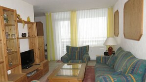 Uma sala de estar com sofá, poltronas, mesa de centro, televisão e um aparador de madeira.