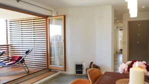 A modern dining area with a wooden table and orange chairs, a large window with blinds, and a view of the city. - Nice Apartment in Diessen (Dießen am Ammersee)