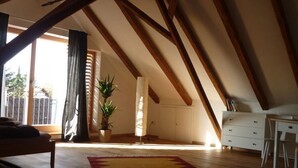 A spacious attic room with exposed wooden beams, a large window, a potted plant, a desk, and a chair. - Nice Apartment in Diessen (Dießen am Ammersee)