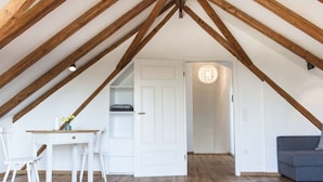 A room with a sloped ceiling, wooden beams, a white door, a desk with chairs, a sofa, and a chandelier. - Nice Apartment in Diessen (Dießen am Ammersee)