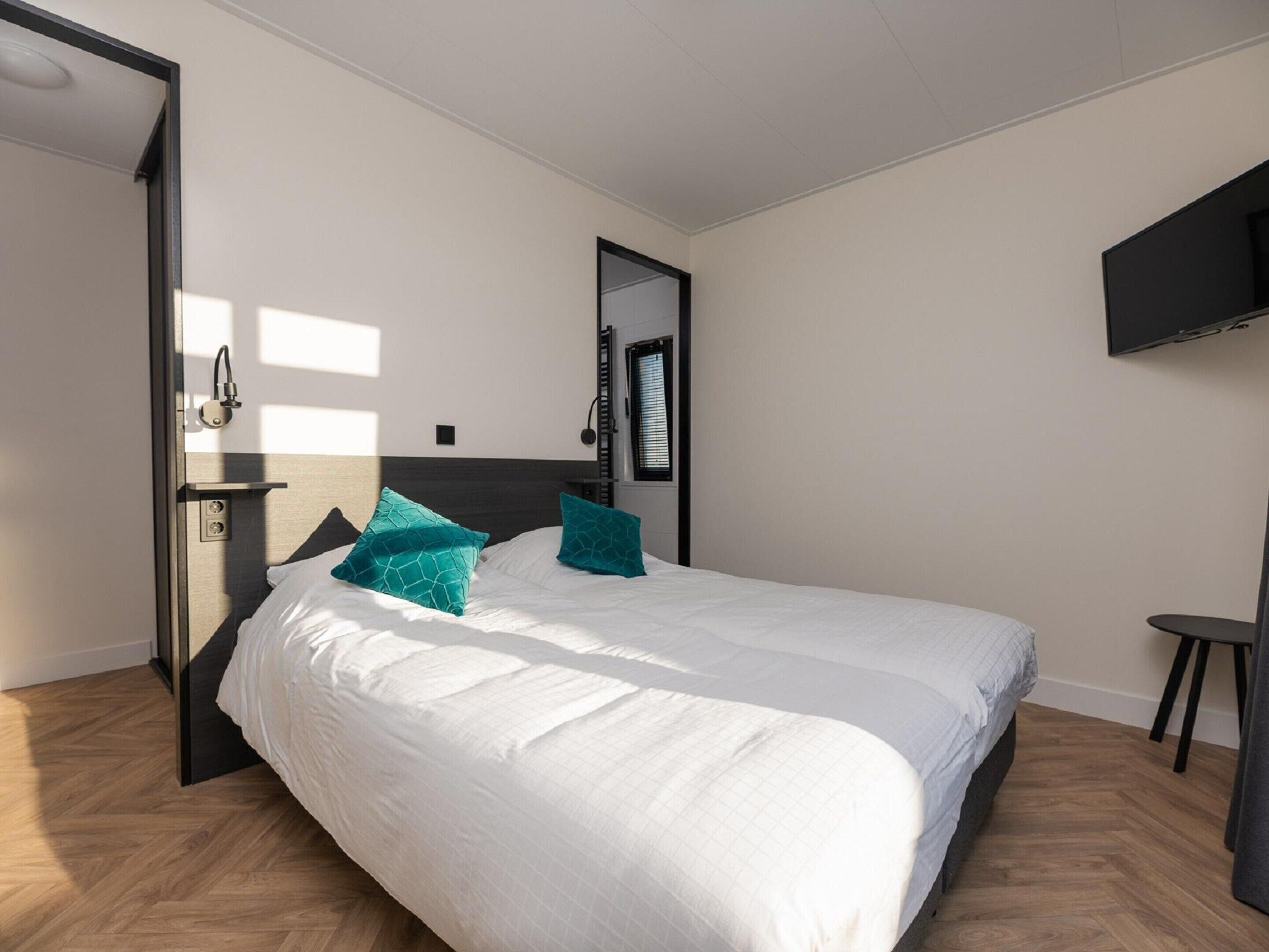 A modern hotel room with a large bed, a TV mounted on the wall, and a door leading to a bathroom.