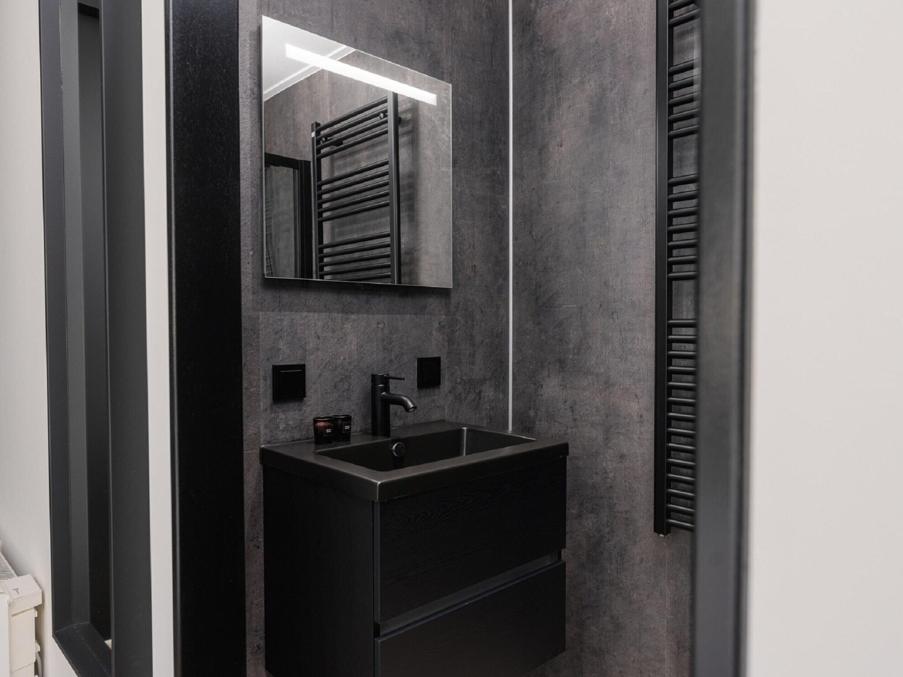 A modern bathroom with a dark sink, a mirror, and a towel rack.