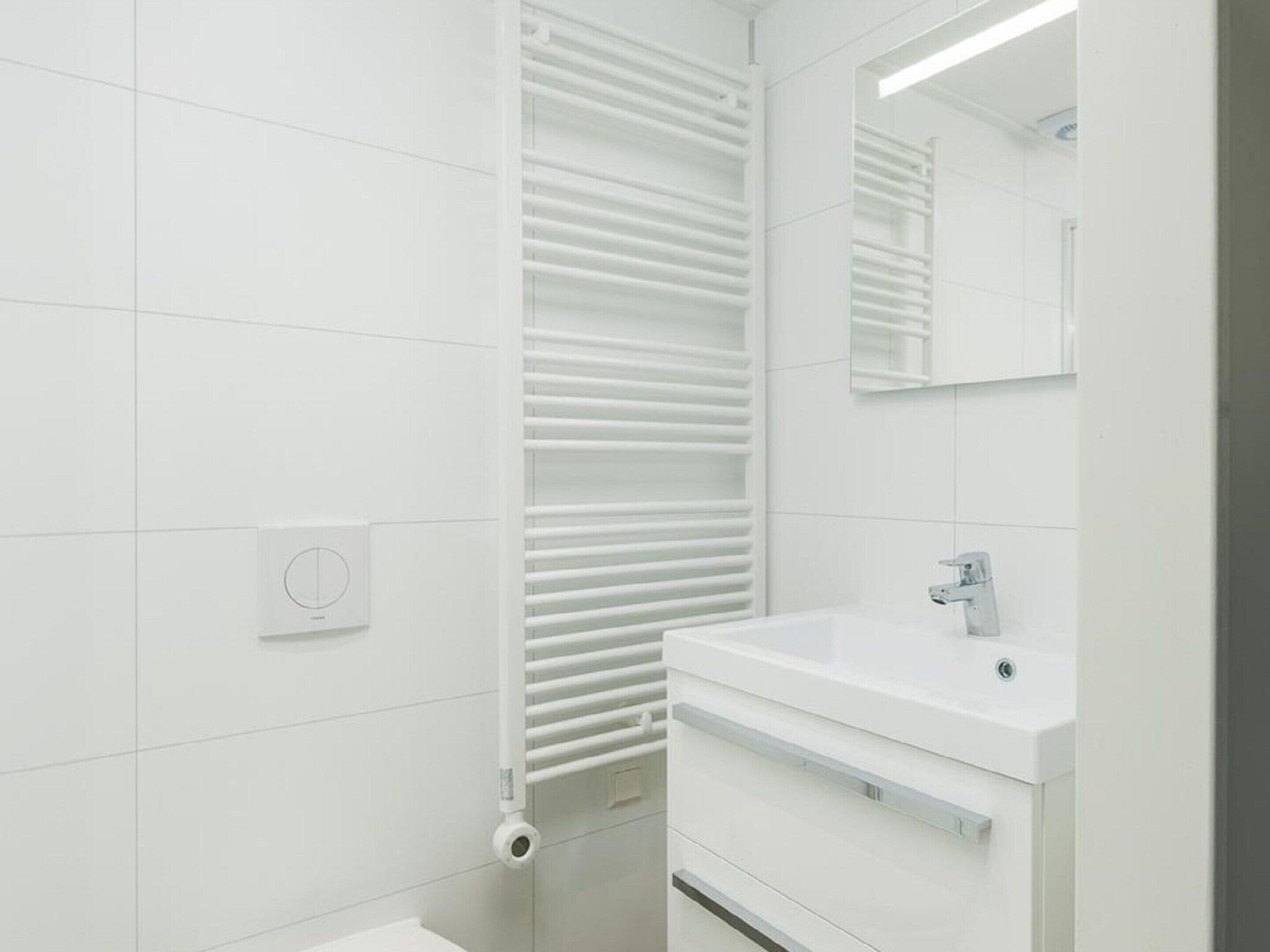Un baño moderno con azulejos blancos, un lavamanos empotrado y un perchero.