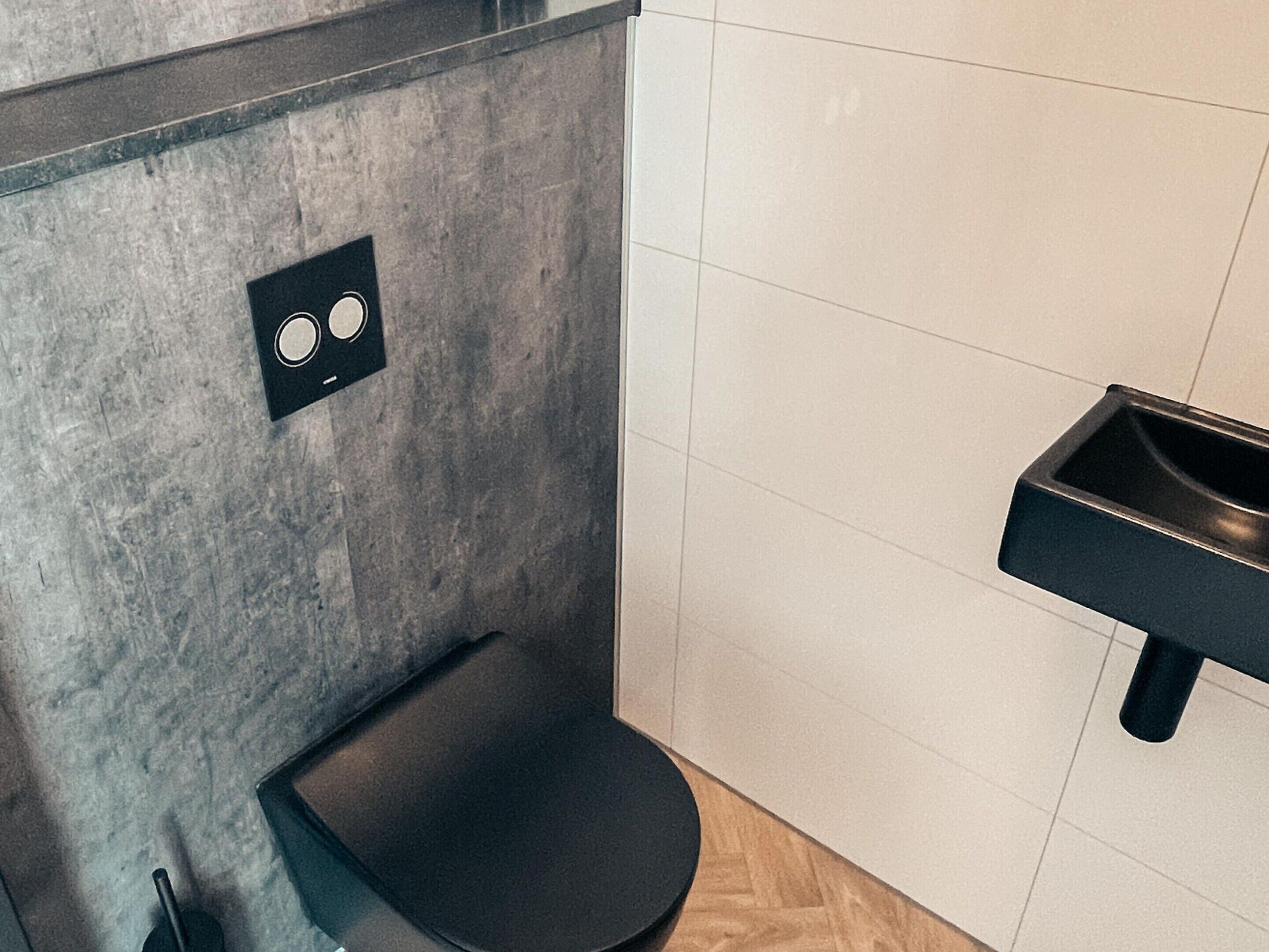 Une salle de bain moderne avec des toilettes noires, un bidet mural et un lavabo.