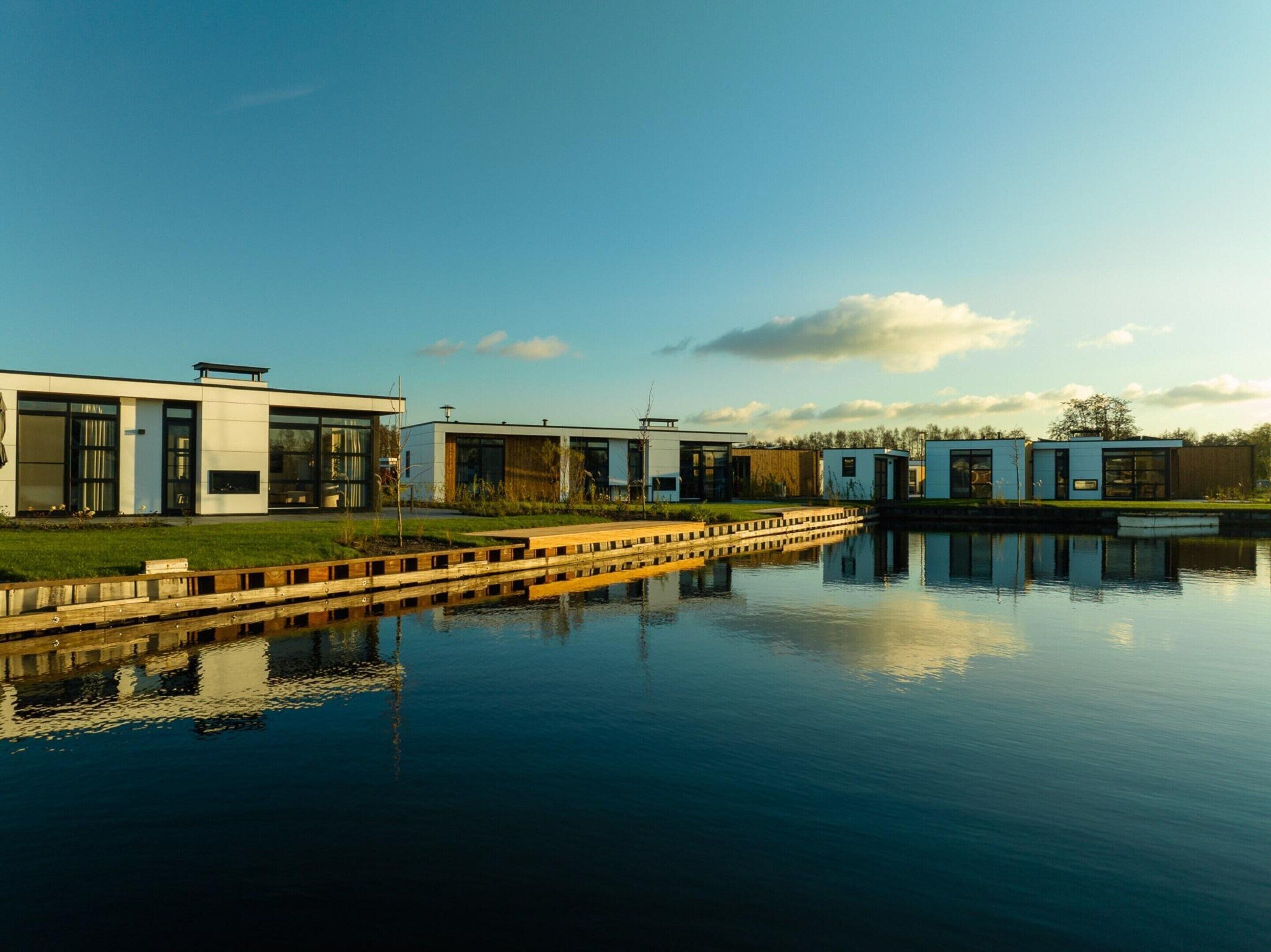 A modern residential area with a canal, featuring contemporary houses with large windows and a wooden walkway along the water.