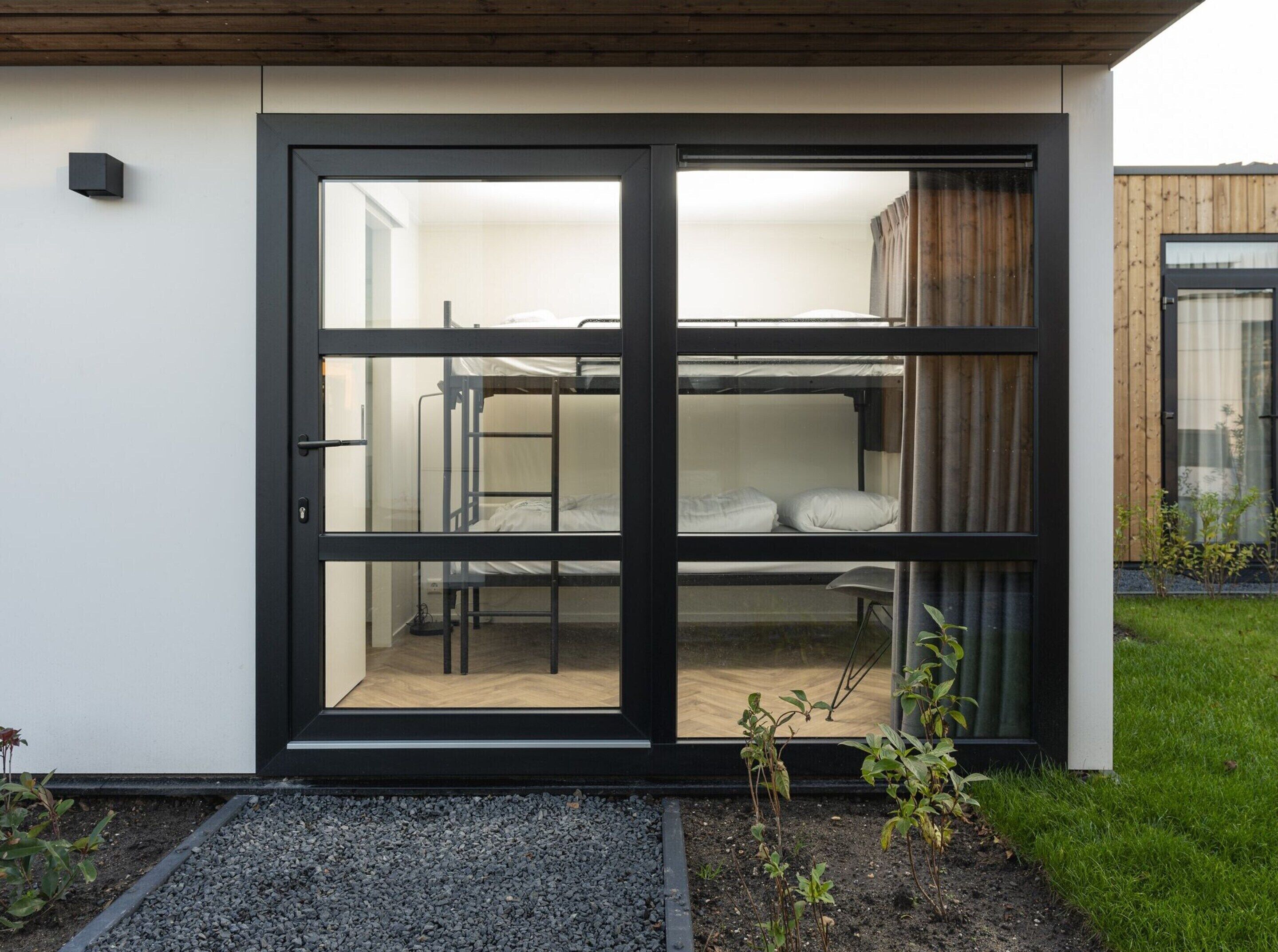 Quarto moderno e compacto com beliches, porta de correr de vidro e um pequeno jardim.