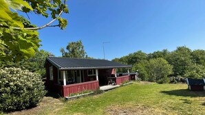 A red cabin with a porch, surrounded by a grassy yard and dense trees. - 5 Person Holiday Home in Nosund-by Traum (Nosund)