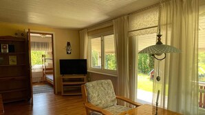 A living room with a television, a wooden chair, a table, and a window with curtains. - 5 Person Holiday Home in Nosund-by Traum (Nosund)