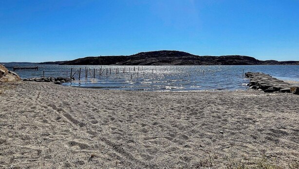 A beach with a rocky shoreline, a wooden pier, and a distant mountain. - 5 Person Holiday Home in Nosund-by Traum (Nosund)