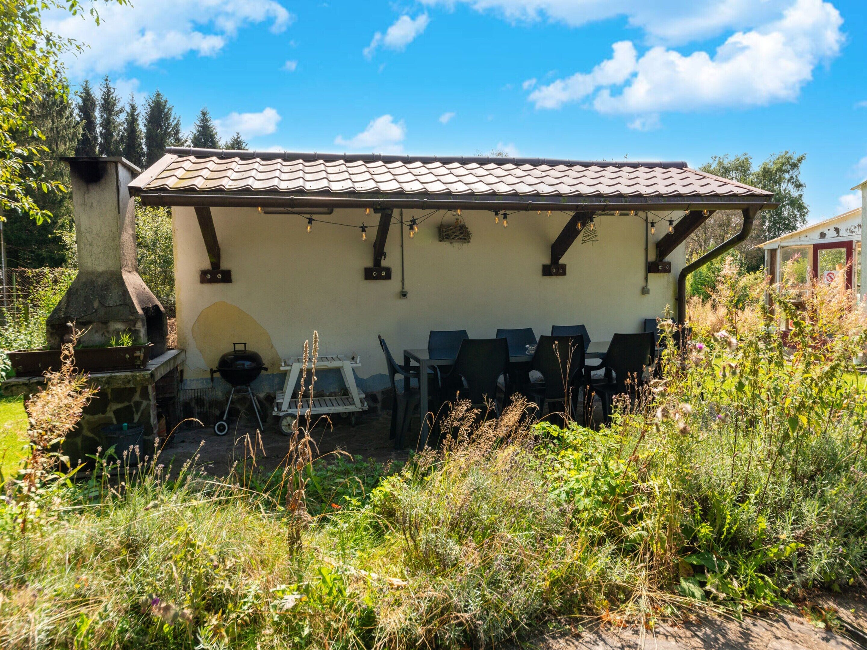 A rustic outdoor seating area with a stone chimney, a grill, and a table with chairs.